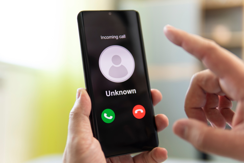 A hand holding a smartphone showing an incoming call with a generic person icon and the label Unknown.