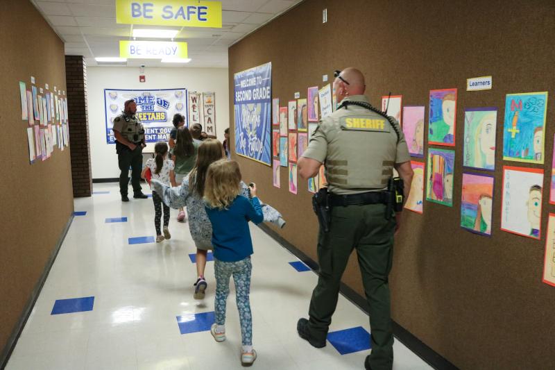 An MCSO SRO walks through a school hall with students.