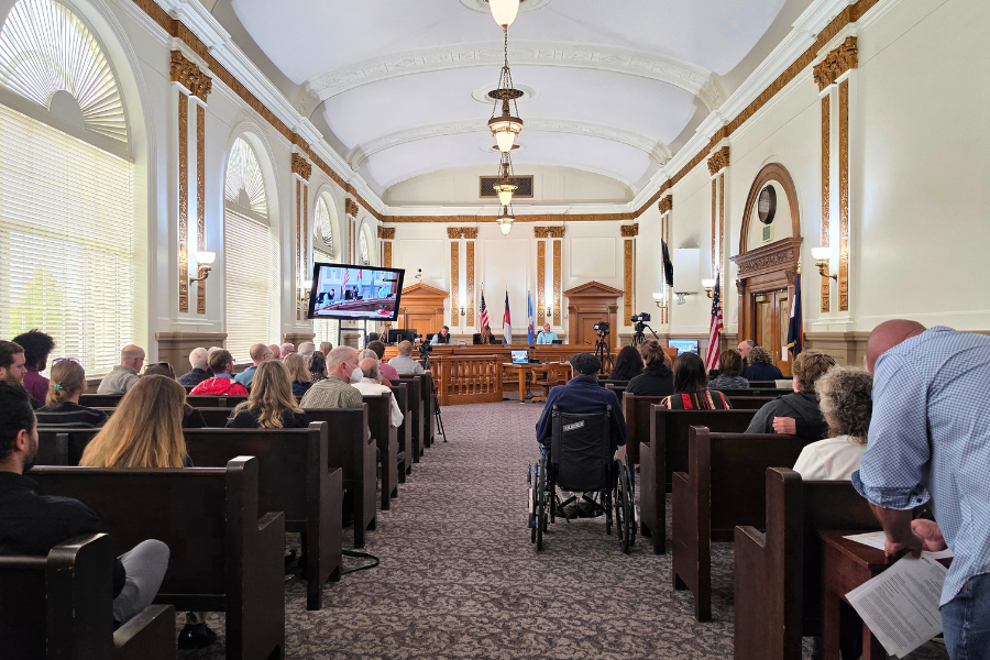 Photo of the public hearing room in the Old Mesa County Courthouse in Grand Junction. Dozens of people sit on benches during a meeting.